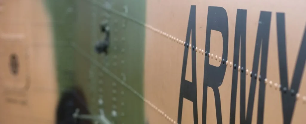 A close-up view of what appears to be the side of an army vehicle or aircraft. The word "ARMY" is inscribed on the surface, and green and beige colours alternate.