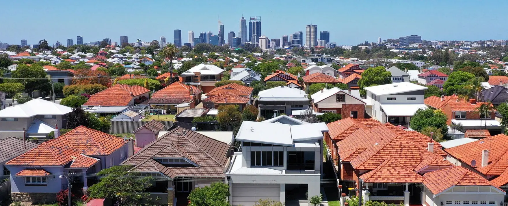 A view over a suburban area. Tightly-packed rooftops cover the foreground, and in the background is the city of Perth skyline